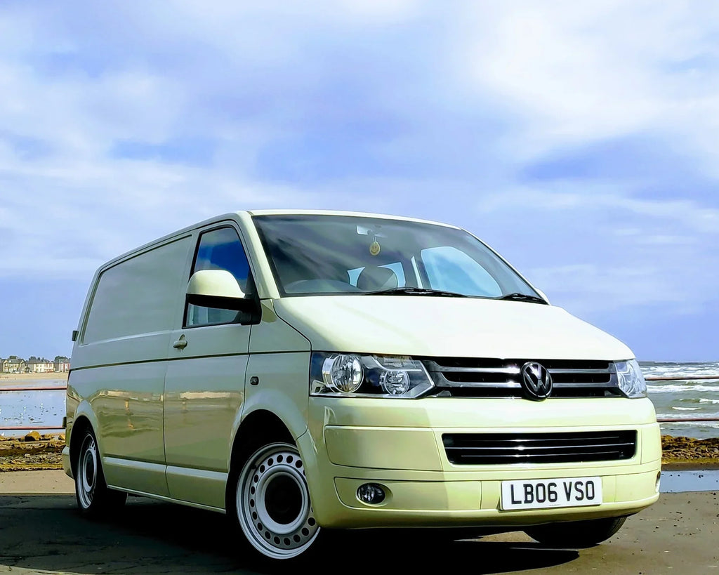 Light-colored van parked on a road with a coastal background